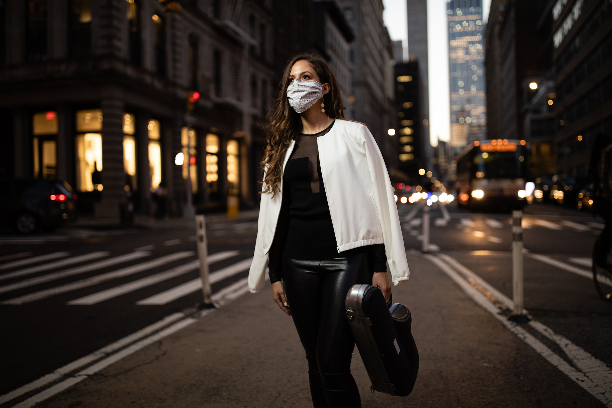 Alexa Tarantino wearing a mask, standing on a street corner in NYC, holding her saxophone case